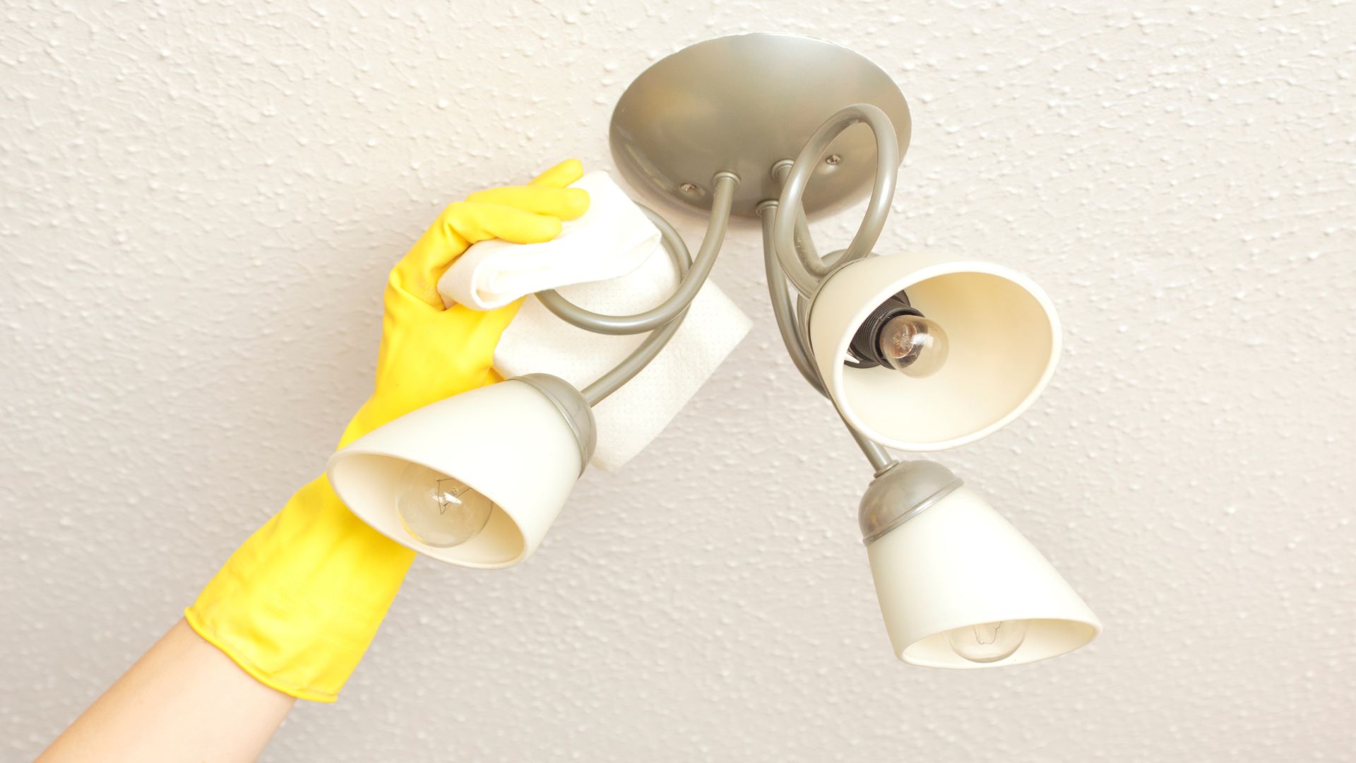 A person wearing yellow gloves and a yellow mitt cleaning a ceiling